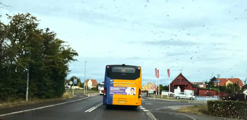 Żółto-niebieski autobus BAT na drodze przy wjeździe do Gudhjem, widok przez mokrą przednią szybę