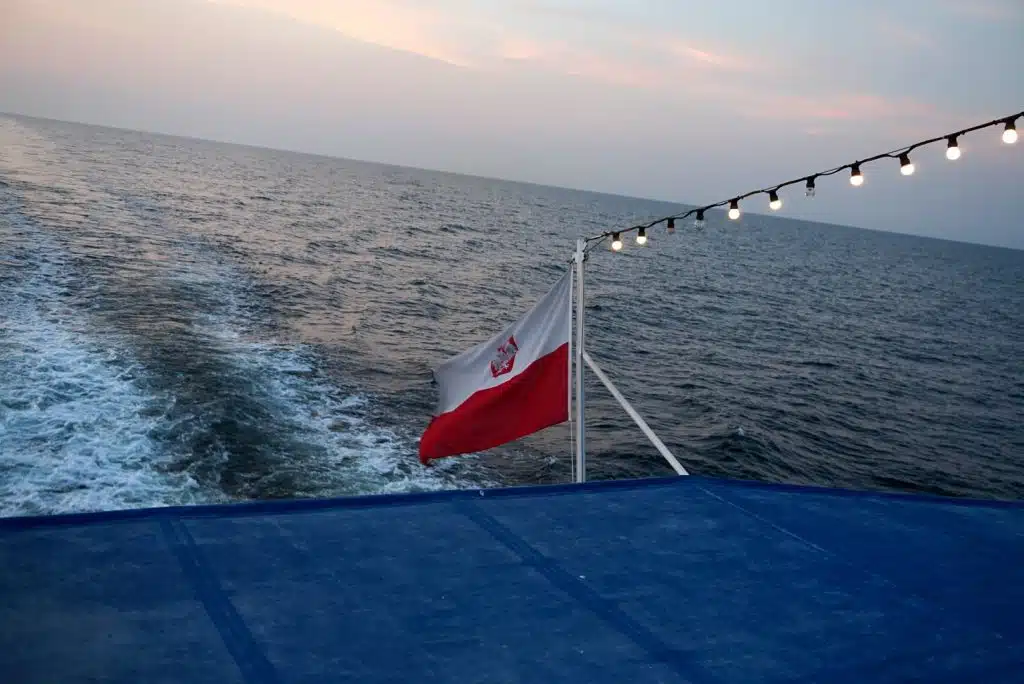 Rejs z Kołobrzegu na Bornholm 2026/2027 – prom, jacht i wycieczki jednodniowe 3 Polska bandera na rufie katamaranu z Nexø do Kołobrzegu o zachodzie słońca