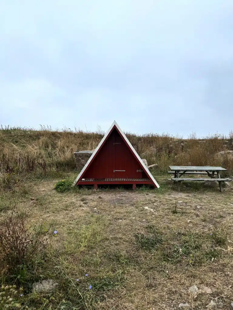 Czerwony shelter w kształcie litery A i drewniany stół piknikowy na trawiastym terenie