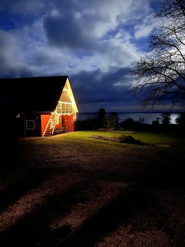 Domek Pyttegården w Gudhjem ze świątecznymi lampkami nocą, w tle Bałtyk